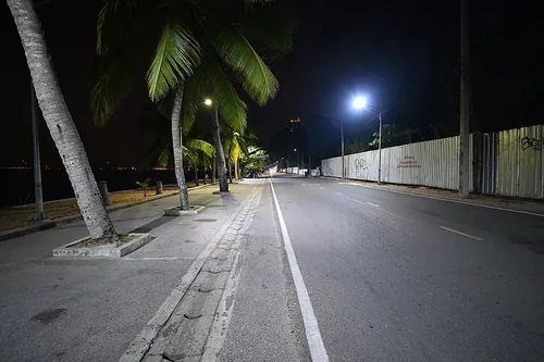 A deserted coastal road stretches into the night in Klet Kaeo, Sattahip District, illuminated by the cool white glow of overhead street lamp