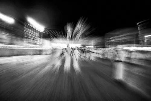 A scene captured in motion, where the silhouettes seem to dissolve into time. The blur transforms the crowd and light into a sensation of sp