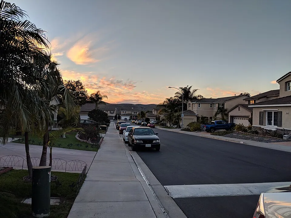 A photograph of the beginning of the sun setting in Oceanside, California. It is taken in a suburb, with a few cars parked along the road. I
